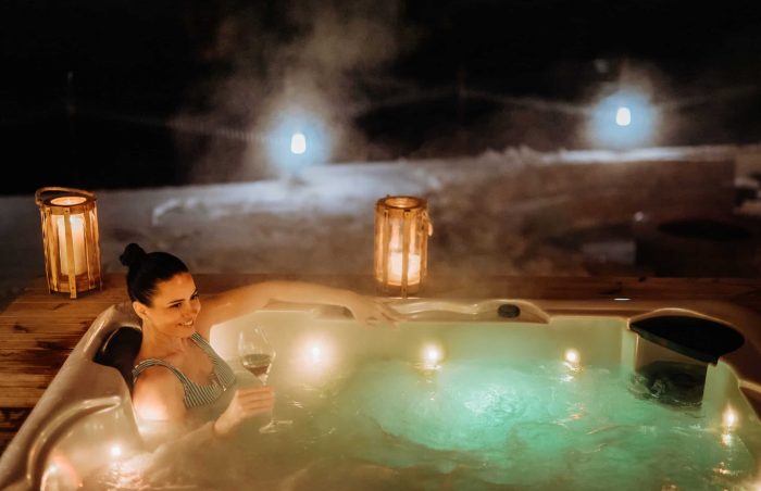 Young woman enjoying outdoor bathtub in her terrace during a cold winter evening.